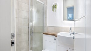 Un baño moderno con ducha envuelta en vidrio, un lavabo blanco y un espejo.