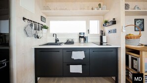 A modern kitchen with a black countertop, a double sink, and a coffee machine. There are cabinets below the countertop and a window above the sink. - BUQEZ ECO RESORT - Villa 47 with breathtaking panoramic views directly on the beach. (Pakoštane)