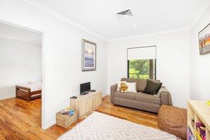 A modern living room with a sofa, a television, and a window with a view of greenery.