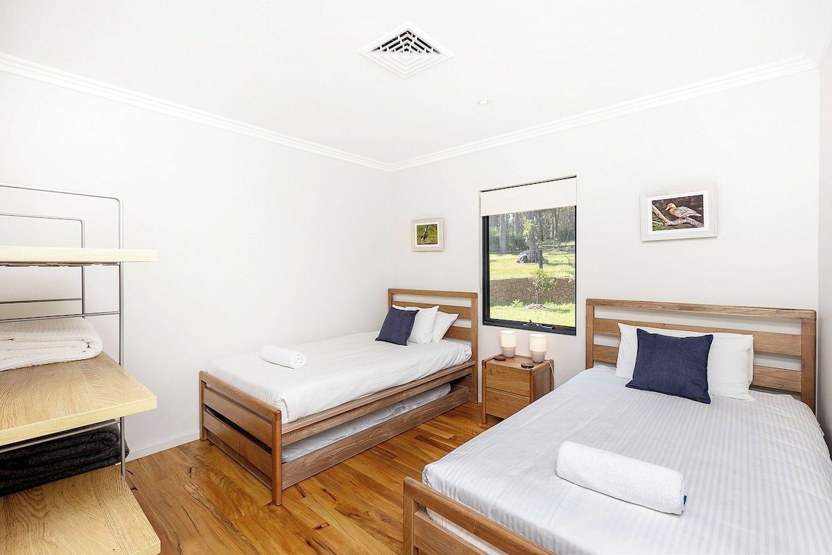 Un dormitorio con dos camas, un escritorio de madera y una ventana con vistas a un bosque.