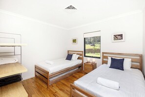 A bedroom with two beds, a wooden desk, and a window with a view of a forest.