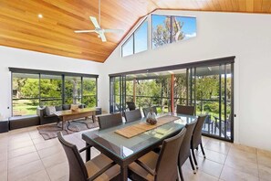 A spacious room with a high ceiling, large windows, a dining table, and a seating area.
