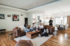 Een moderne woonkamer met een bruine leren bank, een houten salontafel en een eethoek met witte stoelen.