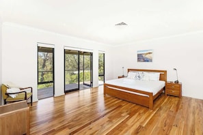 A bedroom with a wooden bed, a nightstand, a chair, and a large window with a view of greenery. - Redgum Treehouse - Luxury home in wine country! (Western Australia)