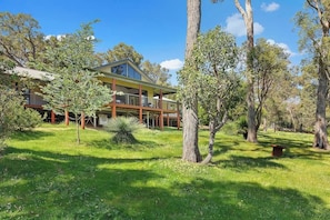 A two-story house with a balcony, surrounded by trees and grass. - Redgum Treehouse - Luxury home in wine country! (Western Australia)