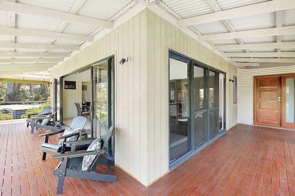 A covered outdoor area with a wooden deck, seating, and glass doors leading to an interior space.