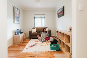 A living room with a sofa, a television, a window, and a bookshelf.