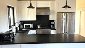 A modern kitchen with white cabinets, a stainless steel refrigerator, a black countertop, and two stools.
