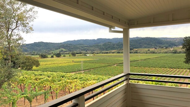 A covered balcony with a view of a vineyard and hills in the background.