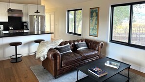 A modern living room with a leather sofa, a coffee table, and a kitchen area with stainless steel appliances.