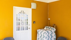 A room with a white door, a bed with a patterned cover, two chairs, and a wall-mounted light fixture. - Falledge Apartments - Pebble (St George)
