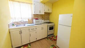 A compact kitchen with white cabinets, a microwave, a stove, and a refrigerator. - Falledge Apartments - Pebble (St George)