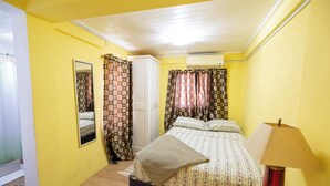 A bedroom with a bed, a bedside lamp, a mirror, curtains, and a wardrobe. - Falledge Apartments - Pebble (St George)