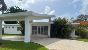 Un edificio moderno con un patio cubierto, un camino de entrada pavimentado y abundante vegetación.