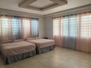 A room with two beds, a tiled floor, and sheer curtains.