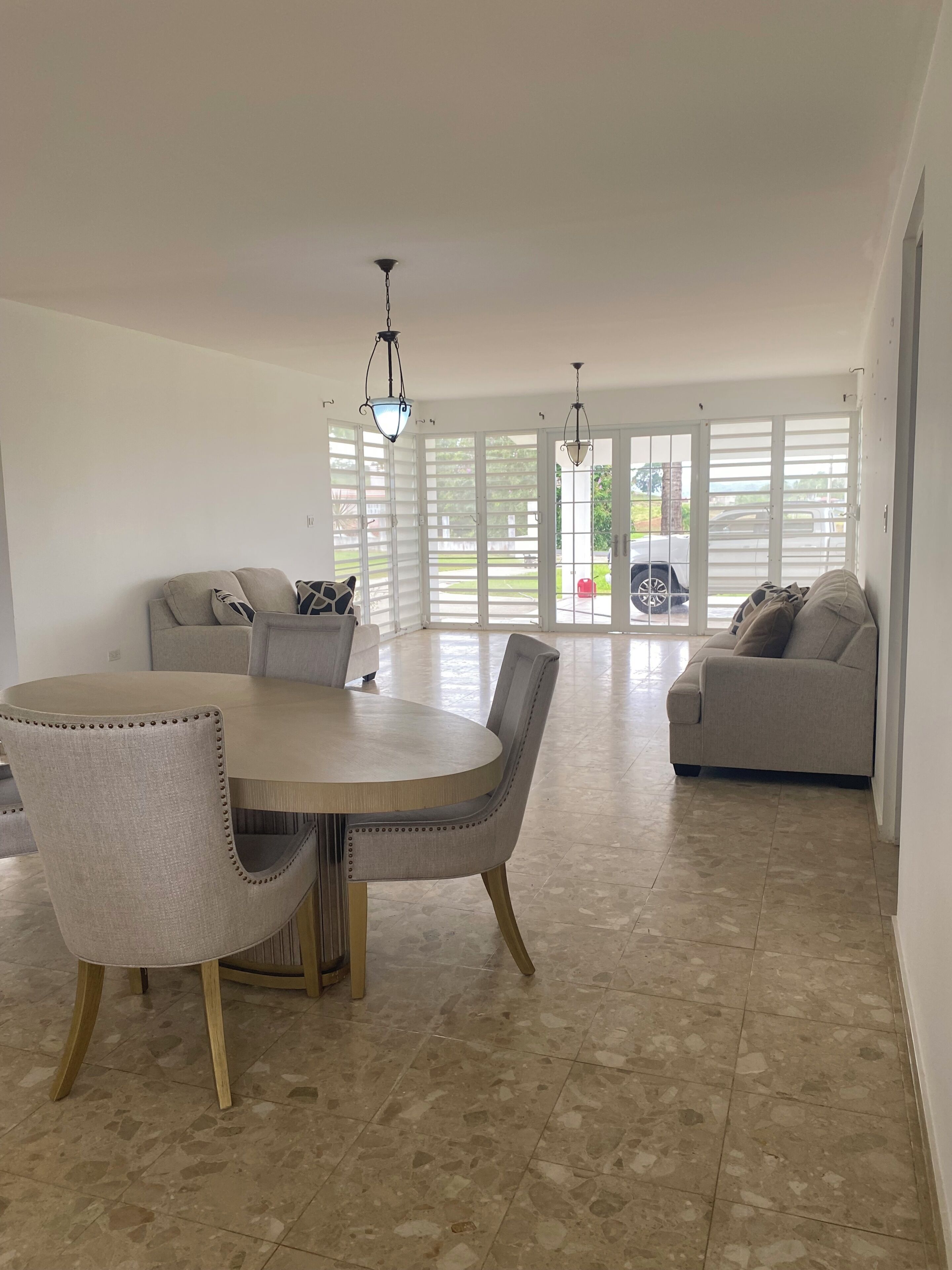 A spacious living area with a round dining table, two sofas, and a view through large sliding doors to the outside.