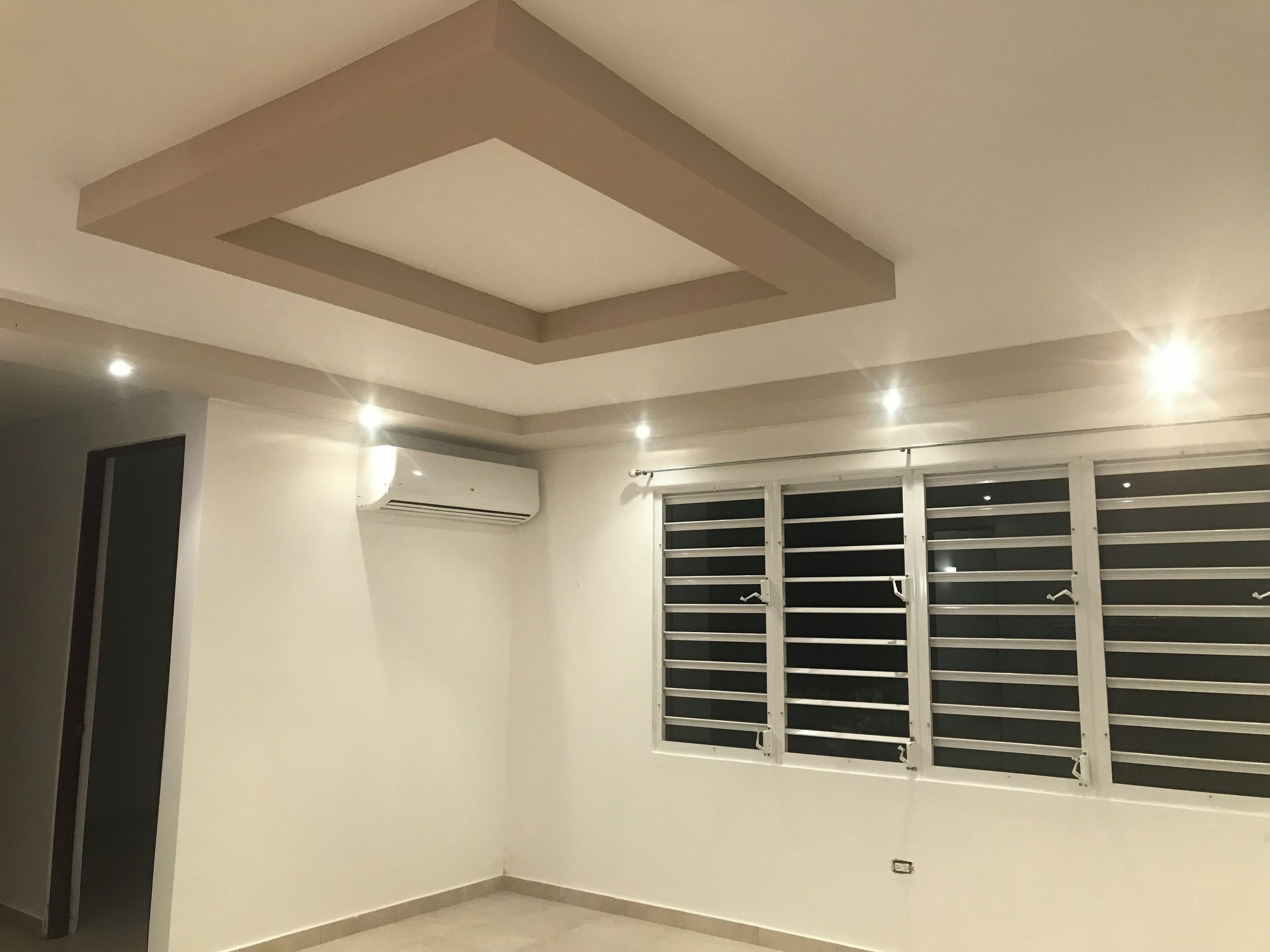 A room with a slatted window, recessed ceiling, and an air conditioning unit.