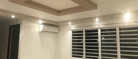 A room with a slatted window, recessed ceiling, and an air conditioning unit.