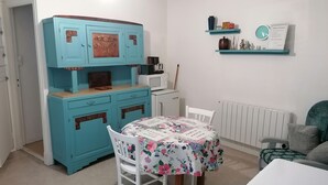 A compact kitchen with a turquoise cabinet, a microwave, and a coffee maker. A table with a floral tablecloth and chairs is in the center. - Charming little art deco apartment (st-claude)