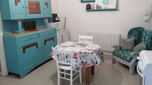 A room with a teal dresser, a white chair, a table with a floral tablecloth, and a bed with a green patterned cover. - Charming little art deco apartment (st-claude)