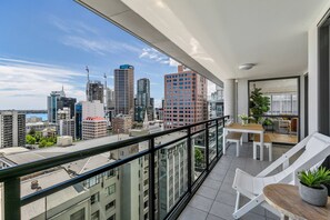 Un balcon avec vue sur la ville, une table à manger, des chaises et une plante en pot.