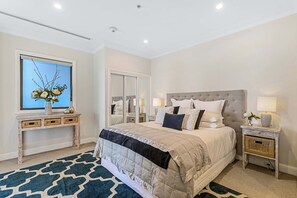 A bedroom with a large bed, a bedside table with a lamp, a mirror, and a console table with decorative items. - Heritage Penthouse with Rooftop Pool & Balcony (Auckland)