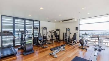 A spacious gym with various exercise equipment, large windows, and a view of the city.