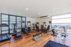 A spacious gym with various exercise equipment, large windows, and a view of the city.