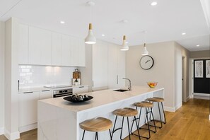 A modern kitchen with white cabinetry, a central island with stools, pendant lighting, and a clock on the wall.