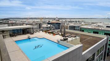 A rooftop pool with a view of the cityscape, including a hotel and construction cranes in the background.