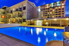 Une piscine à l’eau d’un bleu limpide, entourée d’un bâtiment doté de nombreux balcons et d’un espace de repos abrité.