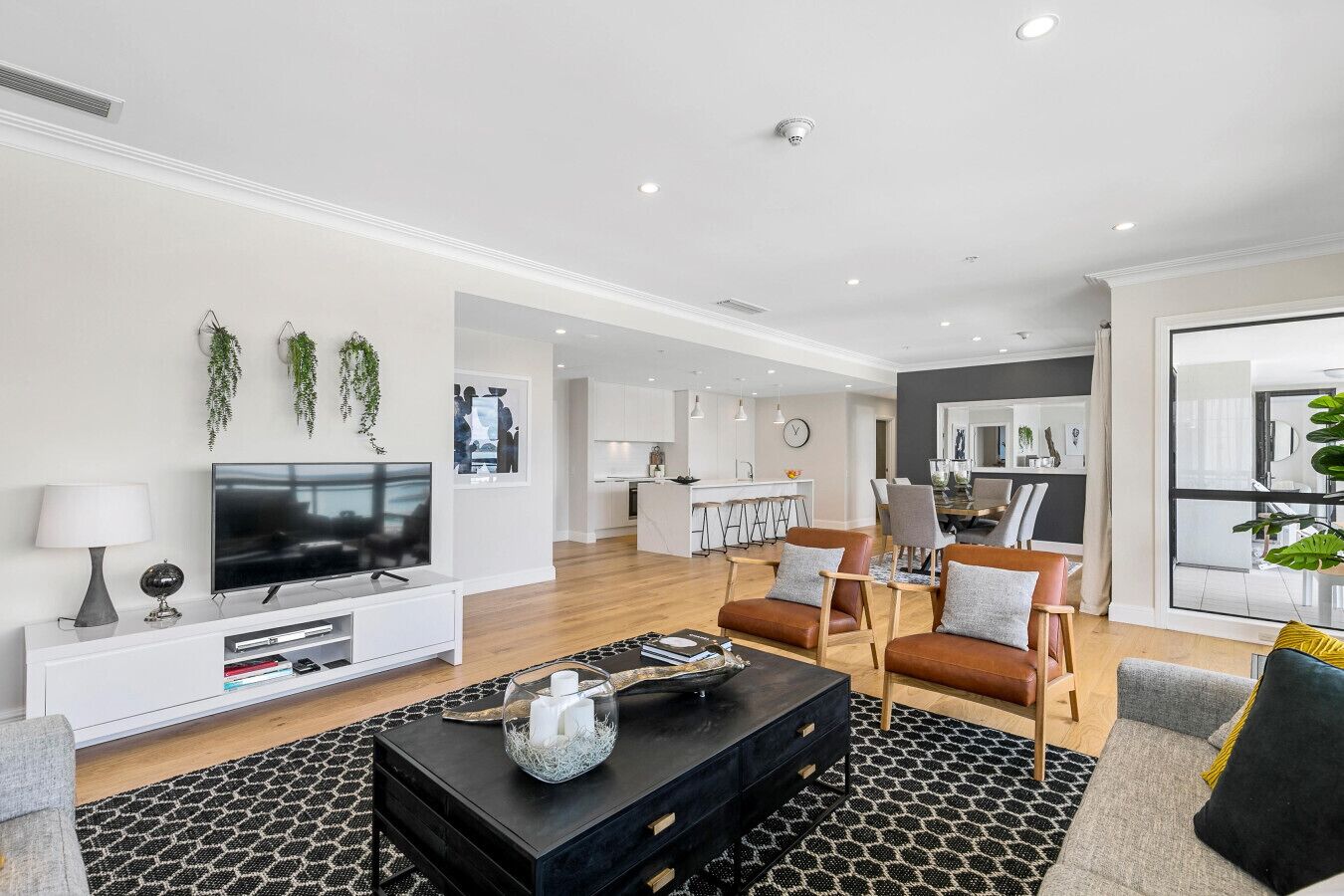 A modern living room with a flat-screen TV, a black coffee table, and leather sofas.