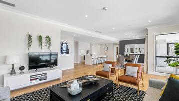 A modern living room with a flat-screen TV, a black coffee table, and leather sofas.