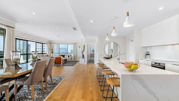 A modern kitchen with a marble countertop, wooden stools, and a fruit bowl.
