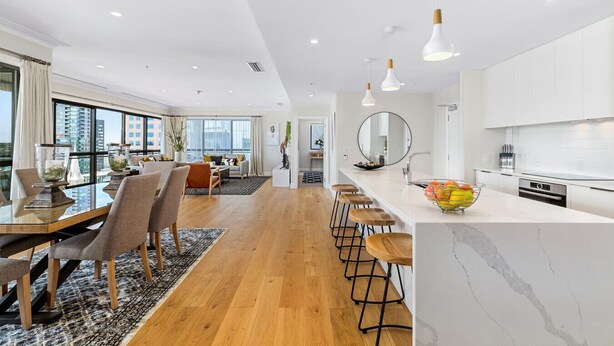 A modern kitchen with a marble countertop, wooden stools, and a fruit bowl.