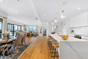 A modern kitchen with a marble countertop, wooden stools, and a fruit bowl. - Heritage Penthouse with Rooftop Pool & Balcony (Auckland)