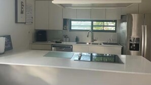 A modern kitchen with white cabinetry, a stainless steel refrigerator, a built-in dishwasher, and a window providing natural light. - Casona Mirimou-Country and Beach House! (Luquillo)