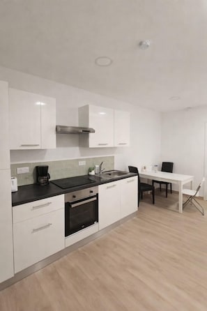 Una cocina moderna con armarios blancos, encimera negra, horno empotrado y comedor con mesa y sillas blancas.