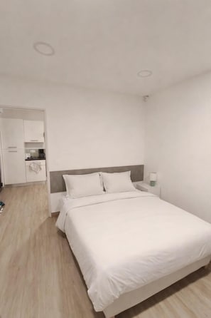 Hotellihuoneessa on sänky, yöpöytä, yöpöydän päällä oleva lamppu, vaatekaappi ja pieni keittotila.