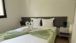 A neatly made bed with a green and white striped blanket, two white pillows, and a decorative swan towel arrangement. - Vacances à la mer apartments climatisés avec terrasse privative (Le Lavandou)