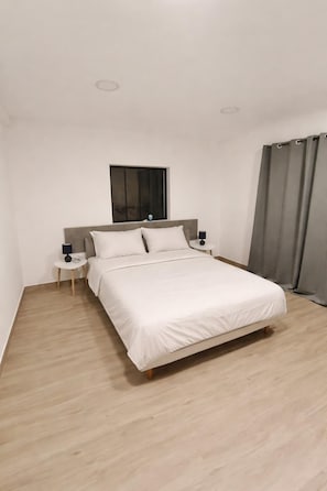 Une chambre d’hôtel moderne avec un grand lit, une petite table de chevet, une commode, une fenêtre et un rideau.