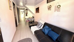 Ein Wohnzimmer mit einer schwarzen Ledersofa, einem Esstisch mit Stühlen, einer Wanduhr und einem Flur, der zu einem anderen Raum führt.