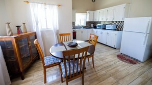 A kitchen with white cabinets, a microwave, and a refrigerator. There is a dining table with chairs and a window with curtains.