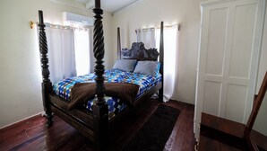 A four-poster bed with a patterned bedspread, a dark wooden floor, and a white door.