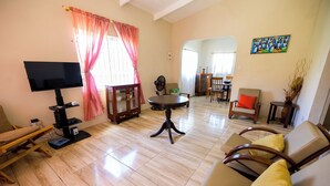 A spacious living room with a flat-screen TV, a round coffee table, and a sofa with yellow cushions.