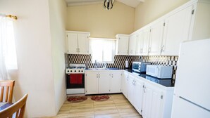 A kitchen with white cabinets, a stove, a microwave, and a refrigerator.