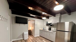 Une cuisine moderne avec un plancher en bois, un réfrigérateur en acier inoxydable et un téléviseur à écran plat fixé au mur.