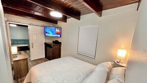 Une chambre à coucher comprenant un lit, un téléviseur fixé au mur, une fenêtre avec des stores et une lampe de chevet.