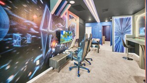 A modern gaming room with a large screen, gaming chairs, and a desk with a monitor. - Mickey Slide • Avengers Room • Star Wars Game Room • Private Pool (Clermont)