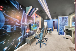 A modern gaming room with a large screen, gaming chairs, and a desk with a monitor. - Mickey Slide • Avengers Room • Star Wars Game Room • Private Pool (Clermont)